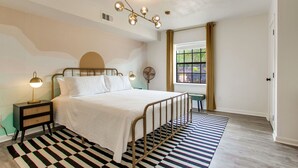 Une chambre à coucher avec un lit, une table de chevet, une lampe et une fenêtre avec des rideaux.
