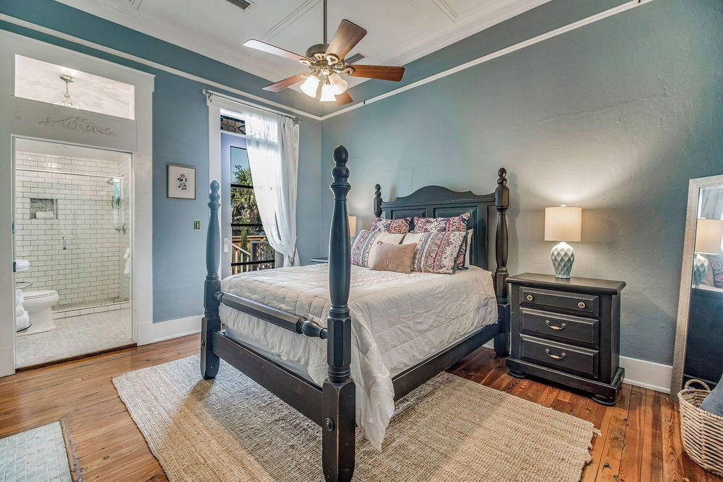 A bedroom with a four-poster bed, a ceiling fan, a nightstand with a lamp, and a view of the bathroom.