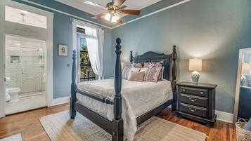 A bedroom with a four-poster bed, a ceiling fan, a nightstand with a lamp, and a view of the bathroom.