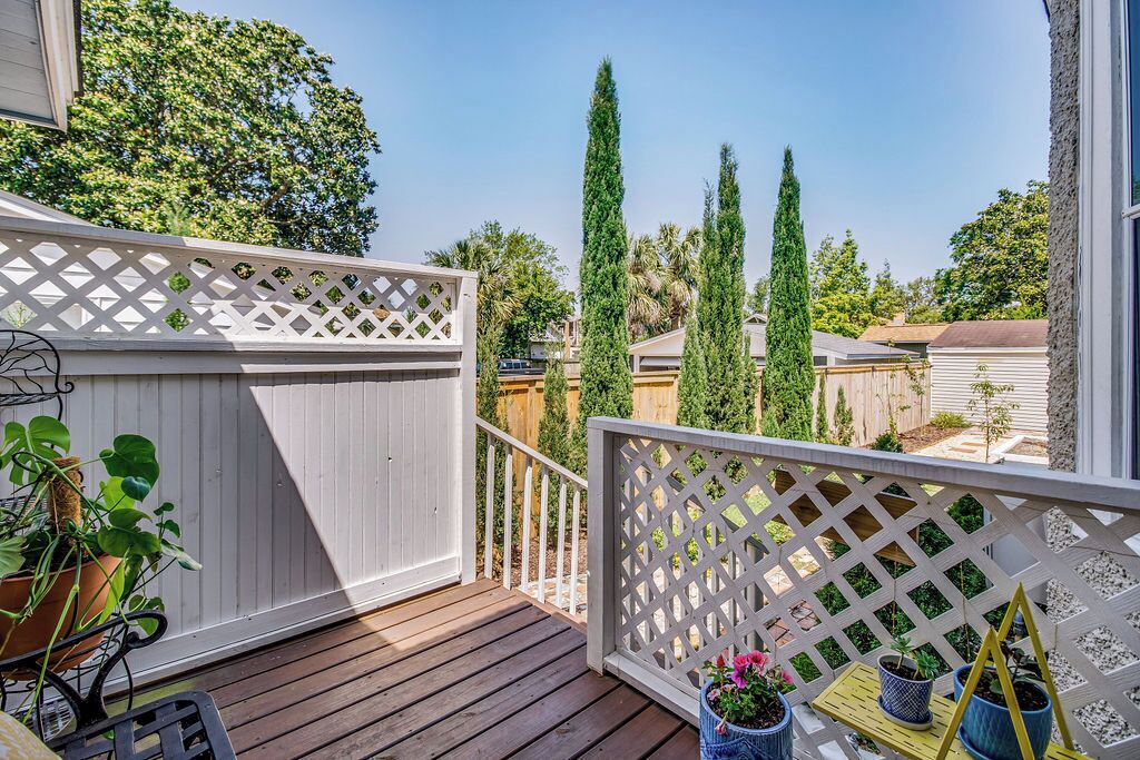 A wooden deck with a white lattice fence, potted plants, and a view of neighboring houses and trees.