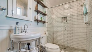 A bathroom with a white sink, toilet, and shower. There are shelves above the sink holding toiletries. - Pensacola 1 BR Sleeps 2 Suite in East Hill (Pensacola)