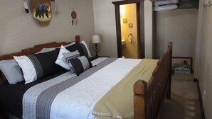 A neatly made bed with a wooden headboard, a bedside table with a lamp, and a wall with a bear painting and a dreamcatcher. - 2 Master Bedrooms-Full Bathrooms /Sleeps 7 /Fully Remodeled /Excellent Condition (Ruidoso)