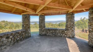 A covered outdoor area with a stone column structure, a concrete floor, and a view of a natural landscape.