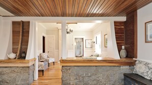A spacious living area with a stone fireplace, wooden ceiling, and a view into another room.