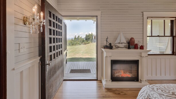 A room with a fireplace, a view through an open door to a grassy area, and a chandelier.