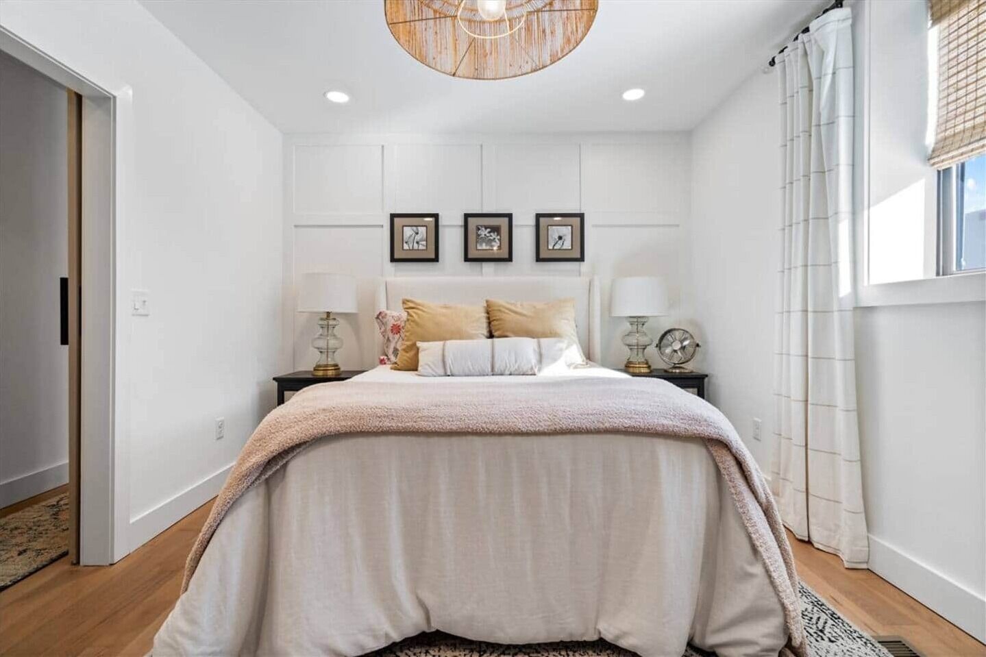 A bedroom with a large bed, two bedside tables with lamps, a ceiling light fixture, and framed pictures on the wall.