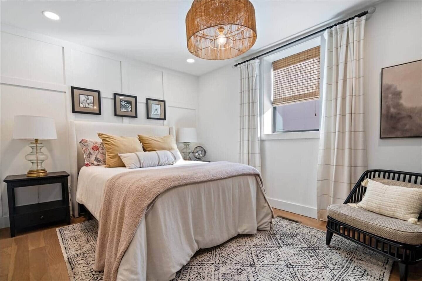 Un dormitorio con cama, mesitas de noche, una lámpara colgante, una ventana con cortinas y una silla.