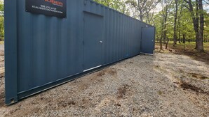 A large, dark blue shipping container with a sign that reads "XCALIBER" and contact information.