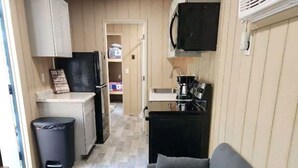 Un espacio habitable compacto con kitchenette, un sofá gris y una pequeña mesa de madera.