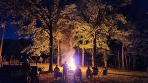 Un grupo de personas sentadas alrededor de una fogata en un área boscosa por la noche.