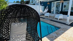 A poolside area with a wicker chair, a hammock, and a glass-enclosed lounge area. - Veranera 1 | Relaxing Private Heated Pool at Aguadilla (Aguadilla)