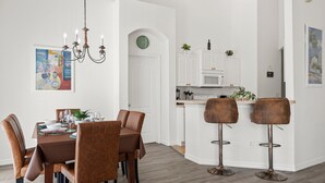A modern kitchen with white cabinets, a dining area with brown chairs, and a bar area with stools. - 293 - Fabulous 3 Bed Villa with Private Oversized Pool (Davenport)