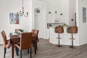 A modern kitchen with white cabinets, a dining area with brown chairs, and a bar area with stools.