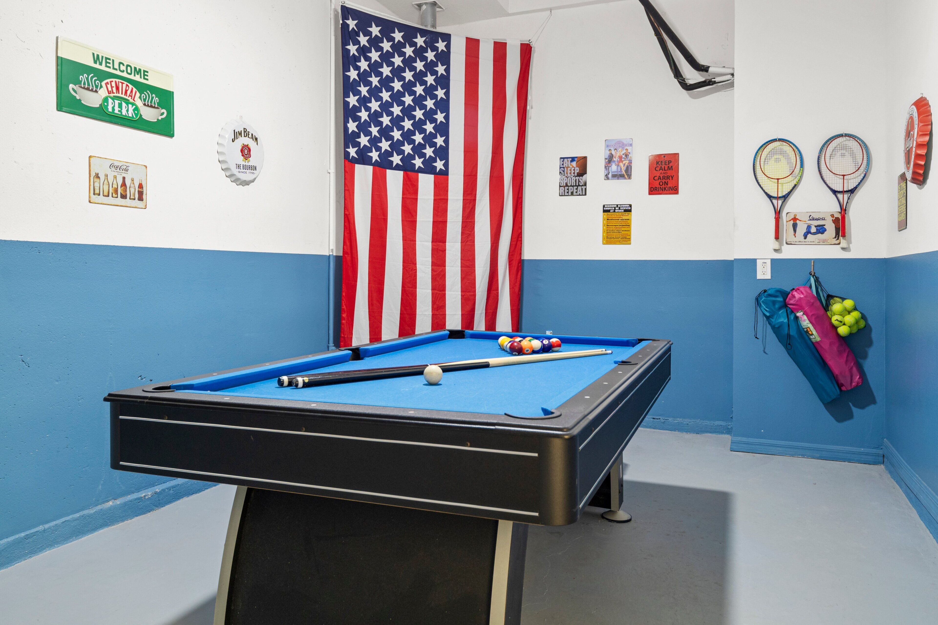 A pool table with balls, an American flag, and various wall decorations including a welcome sign and a Coca-Cola sign.