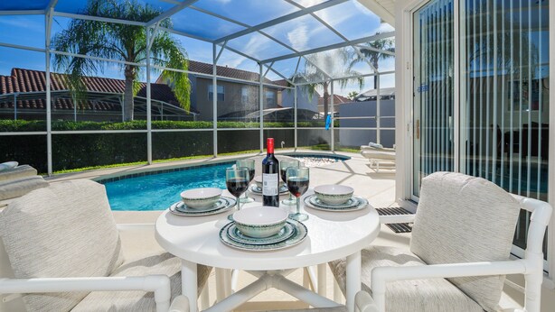 A covered outdoor patio with a pool, white furniture, and a bottle of wine. - 293 - Fabulous 3 Bed Villa with Private Oversized Pool (Davenport)