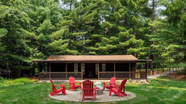 A covered outdoor area with a wooden deck, red Adirondack chairs, and a fire pit.