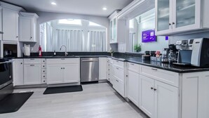 Une cuisine moderne avec des meubles blancs, un lave-vaisselle en acier inoxydable, un coin café et un plan de travail noir.