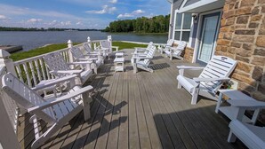 Une terrasse en bois avec des fauteuils Adirondack blancs, un bâtiment en pierre et une vue sur un lac.