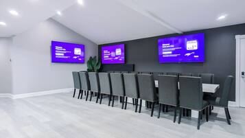 Una sala conferenze con un lungo tavolo, diverse sedie e tre grandi schermi a parete che mostrano informazioni.