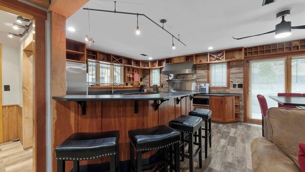 A modern kitchen with wooden cabinetry, a central island with stools, and a dining area with a red chair. - Private I Pool Table I Bar I Studio I House I Roku (Westerville)