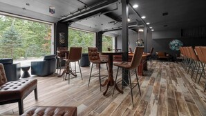 A modern interior with a large dining table, leather chairs, and a view of trees through large windows. - Private I Pool Table I Bar I Studio I House I Roku (Westerville)
