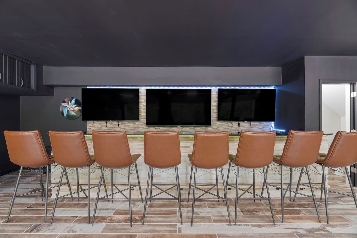 A room with six brown chairs arranged in a row, a flat-screen TV mounted on the wall, and a decorative circular piece on the wall.