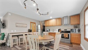 A modern kitchen with wooden cabinets, a central island, and a dining area with a round table and chairs.