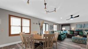A spacious living room with a dining area, a ceiling fan, and a large window with blinds.