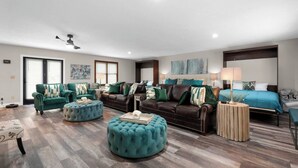 A spacious living area with a large sofa, ottomans, and a separate bedroom with a bed and nightstand.