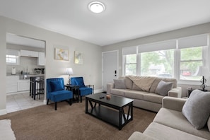 A modern living room with a sofa, two armchairs, a coffee table, and a kitchen in the background.