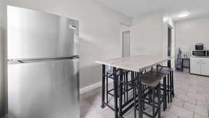 Eine moderne Küche mit einem Edelstahl-Kühlschrank, einem Holztisch mit Barhocker und einer Mikrowelle in einem weißen Schrank.