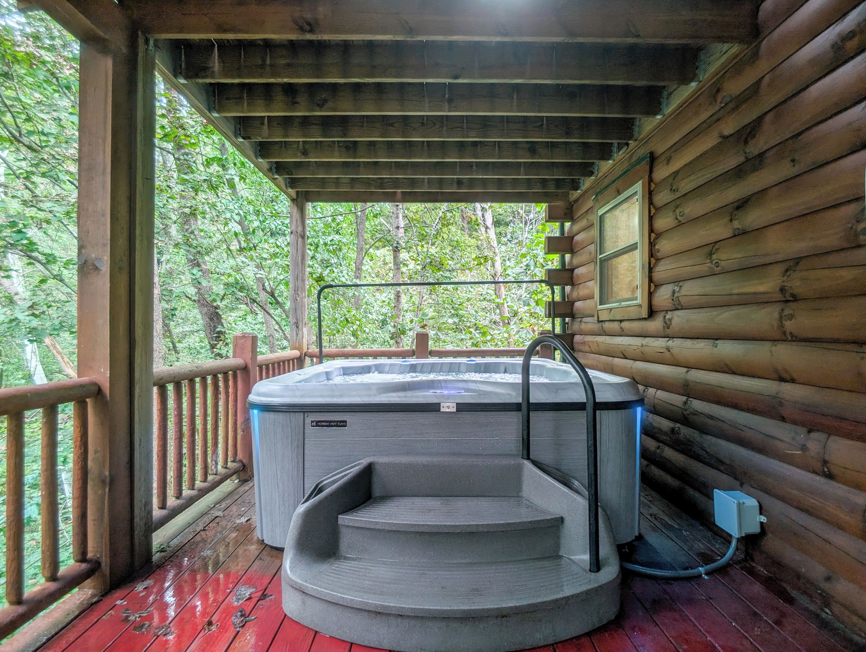 A hot tub on a wooden deck with a wooden railing, surrounded by trees.