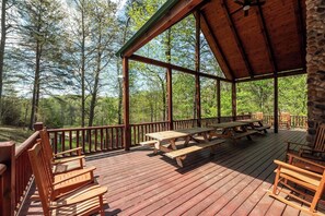 Une terrasse extérieure couverte, dotée de tables et de chaises pour pique-niquer, et entourée d’arbres.