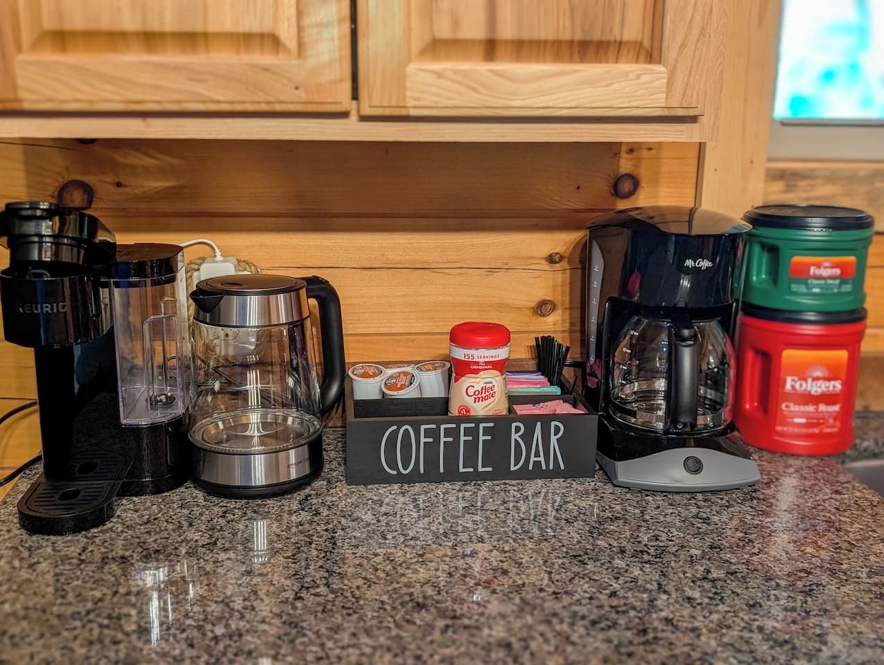 A coffee bar setup with a Keurig machine, a coffee maker, Folgers coffee, and a coffee mug on a granite countertop.