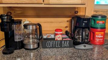 A coffee bar setup with a Keurig machine, a coffee maker, Folgers coffee, and a coffee mug on a granite countertop.