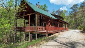 A log cabin with a porch, surrounded by trees. - Spacious | Sleeps 22 | Pool Table, EV Charger,King (Logan)