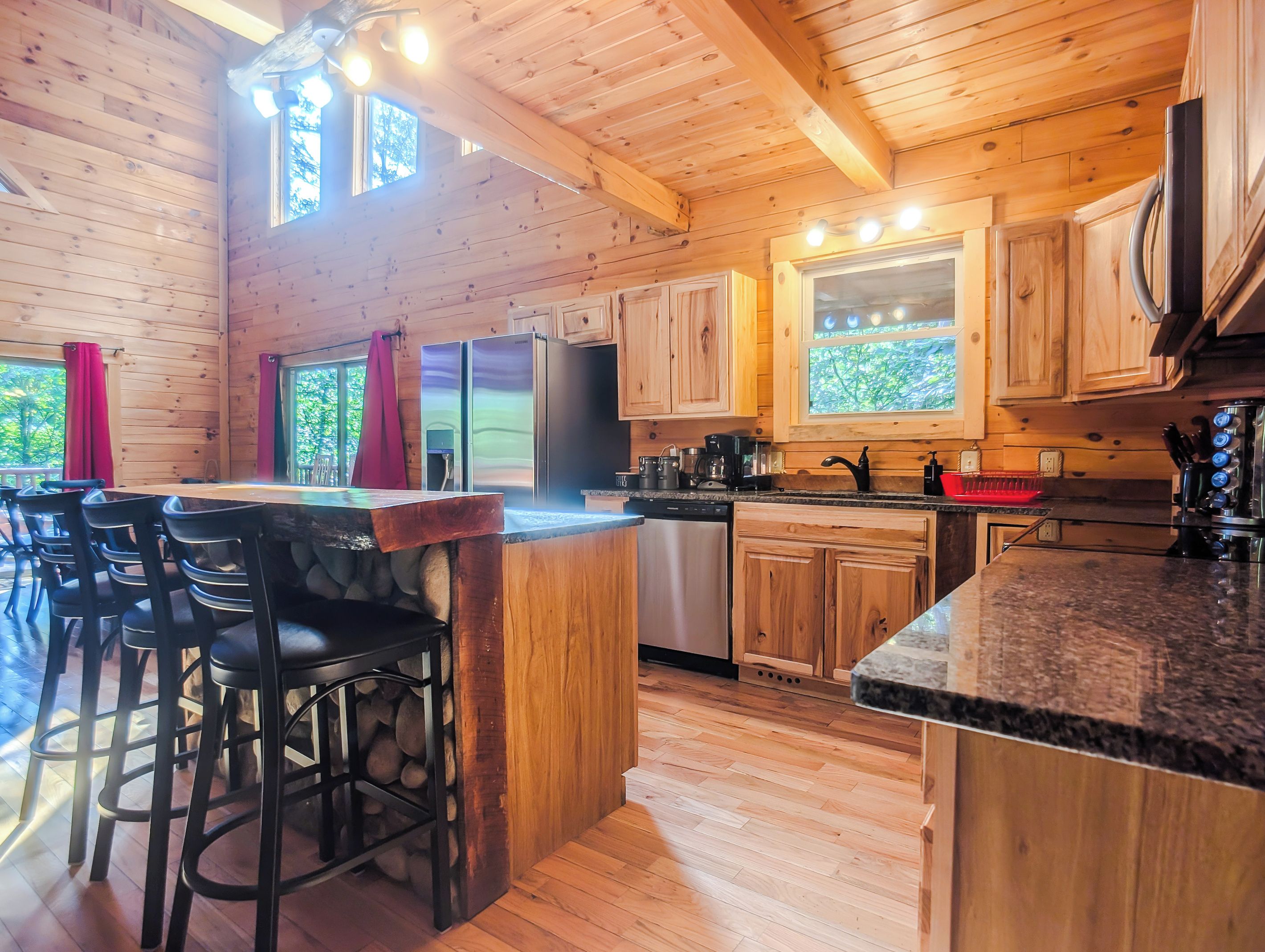 A wooden interior with a kitchen area, bar stools, and a dining table.