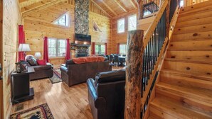 A log cabin interior with a fireplace, wooden floors, a staircase, and a dining area. - Spacious | Sleeps 22 | Pool Table, EV Charger,King (Logan)