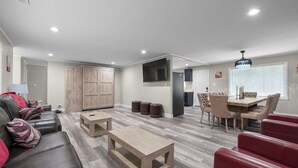 A spacious living area with a sofa, coffee table, and red chairs, a dining table with chairs, and a kitchen area with cabinets and a TV. - Pool Table • Fire Pit • Bar • King • Sleeps 22 (Galena)