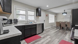 A modern kitchen with a microwave, sink, and cabinets, a dining area with chairs and a table, and a red rug on the floor. - Pool Table • Fire Pit • Bar • King • Sleeps 22 (Galena)