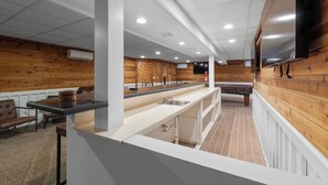 A modern kitchen with a long counter, wooden paneling, and a flat-screen TV mounted on the wall. - Pool Table • Fire Pit • Bar • King • Sleeps 22 (Galena)