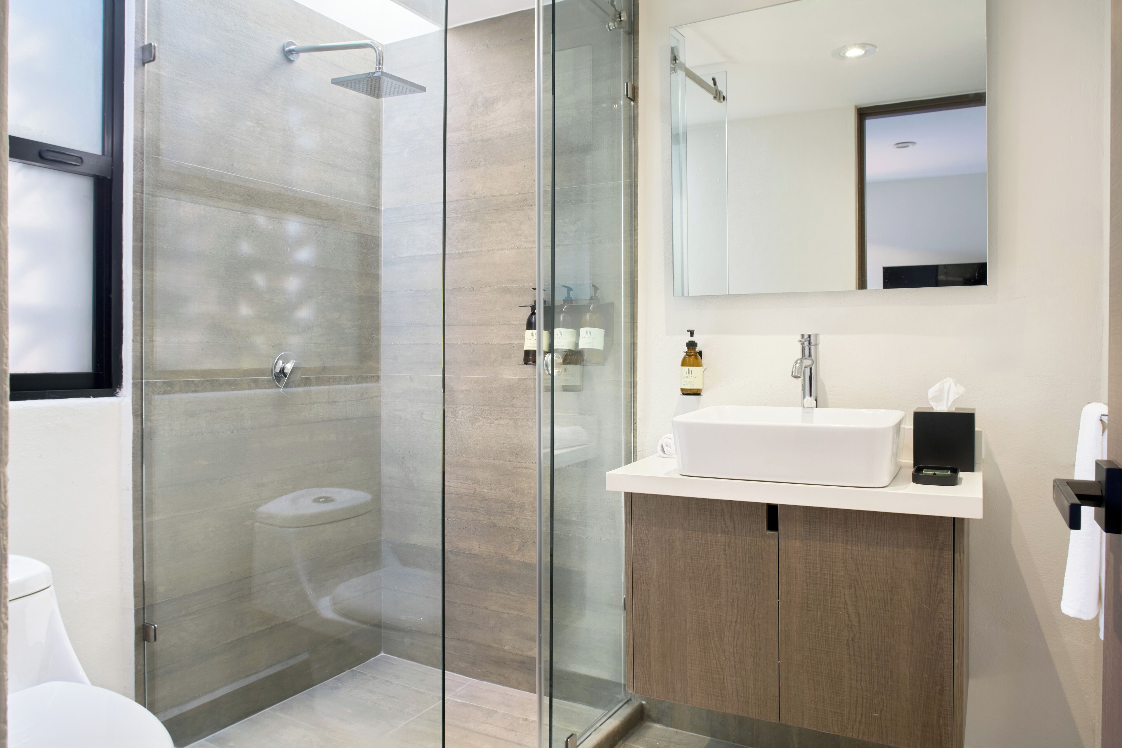 A modern bathroom with a glass-enclosed shower, a white sink, and a wooden vanity.