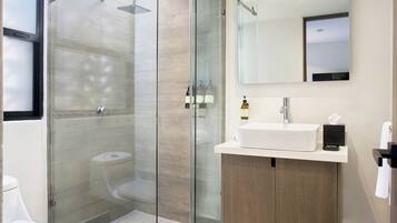 Een moderne badkamer met een douchecabine van glas, een witte wastafel en een houten opbergmeubel.