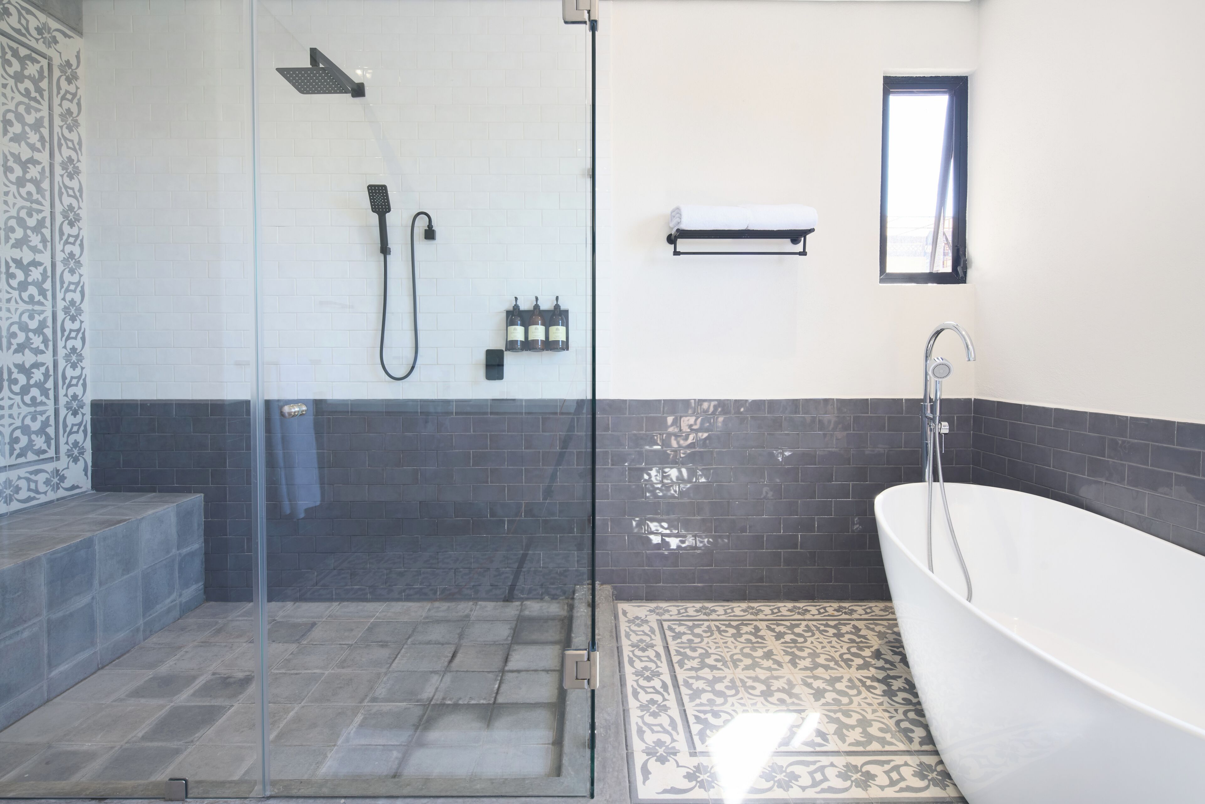 Ein modernes Badezimmer mit einer Glastrennwand zur Dusche, einer freistehenden Badewanne und einem kleinen Fenster.