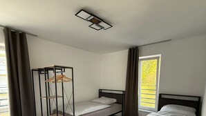 A bedroom with two single beds, a wooden wardrobe, and a window with curtains. - StayEasy Accommodation (Gummersbach)