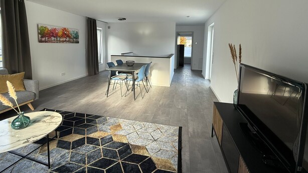 A modern living room with a dining area, a flat-screen TV, and a view into the kitchen. - StayEasy Accommodation (Gummersbach)