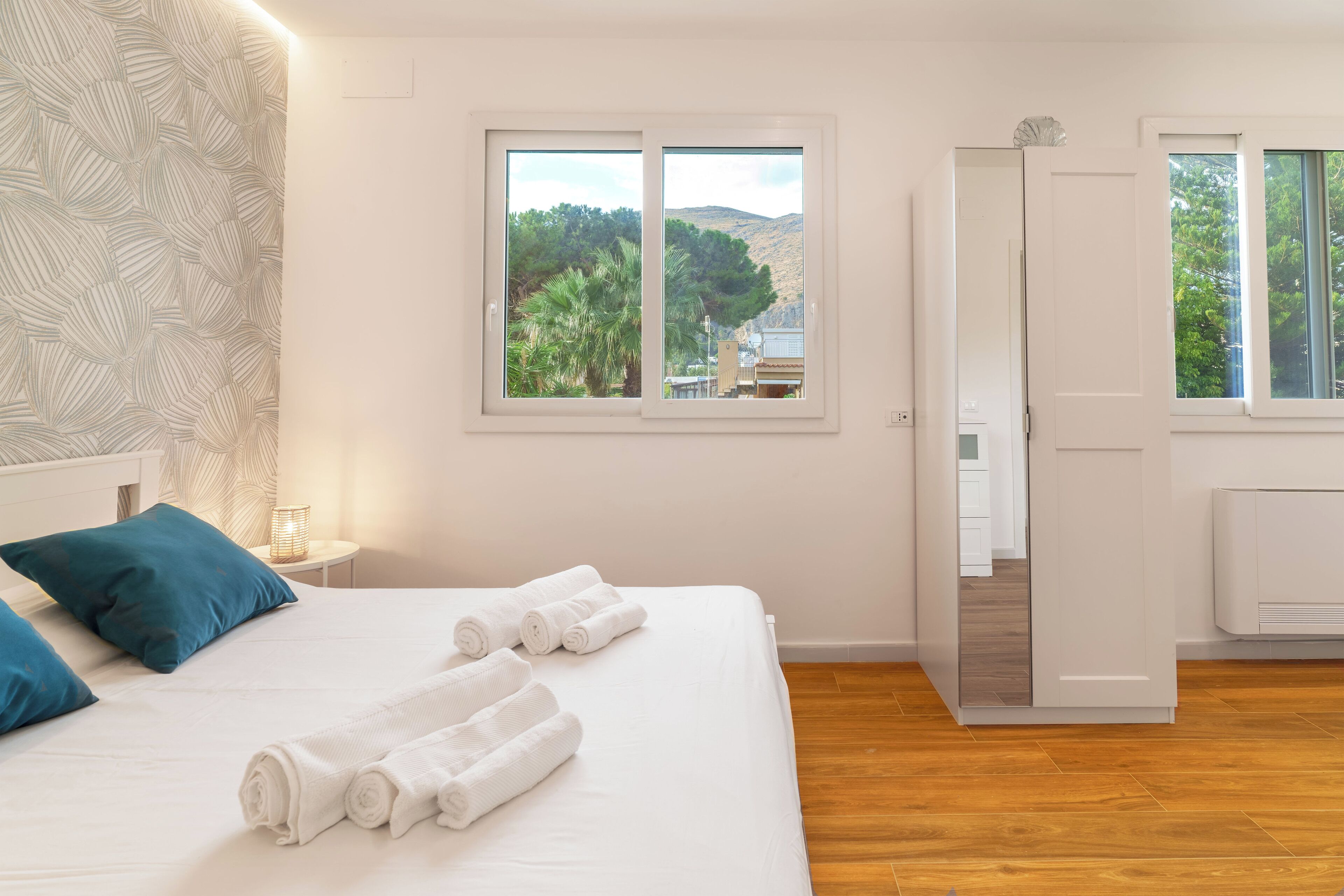 A hotel room with a bed, two windows, and a view of trees and hills.