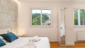 Ein Hotelzimmer mit Bett, zwei Fenstern und Blick auf Bäume und Hügel.