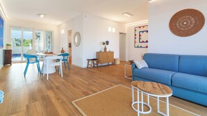Ein modernes Wohnzimmer mit einem blauen Sofa, Holzböden, einem Essbereich mit blauen Stühlen und einem großen Fenster.