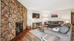 Ein Wohnzimmer mit Steinwand, Kamin, einer Couch, einem Couchtisch und einem an der Wand befestigten Fernseher.